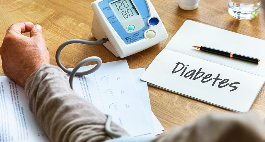Person checking for diabetes symptoms beside a blood glucose monitor and diabetes notes