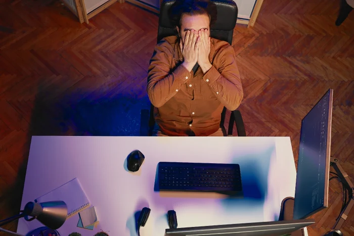 Overhead view of a remote worker at a computer desk appearing exhausted during late night work hours in a home office